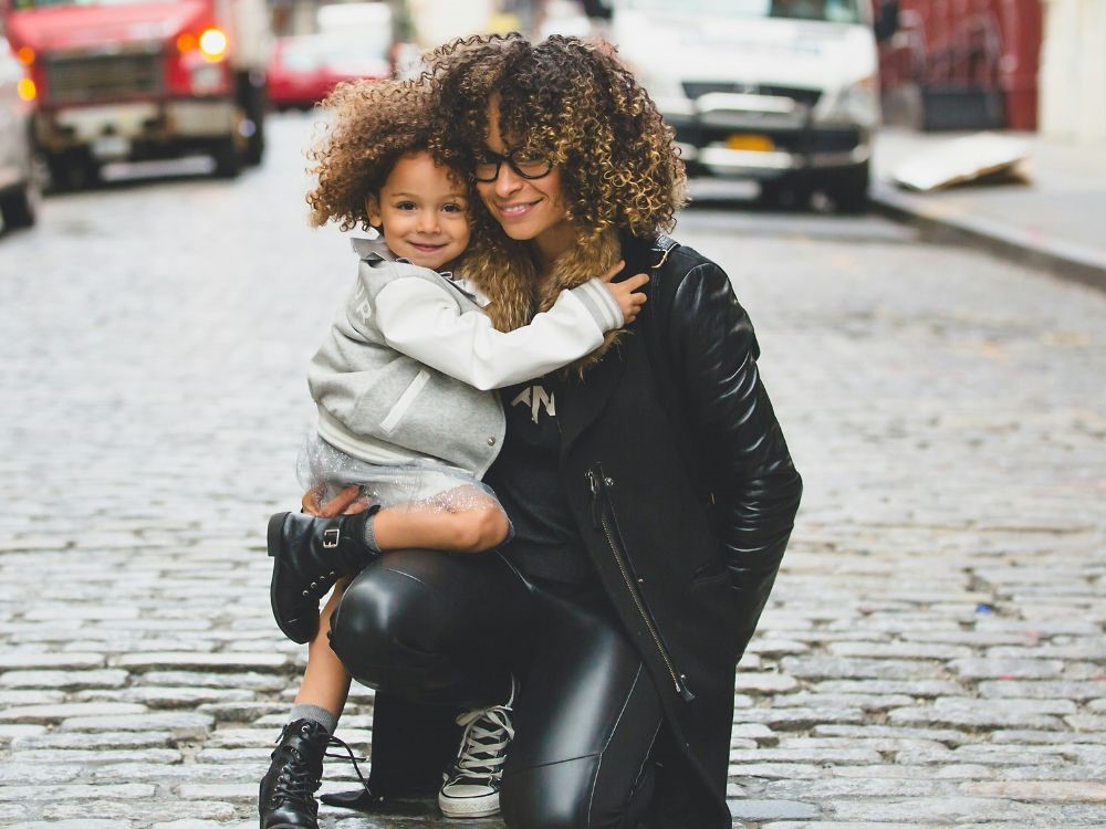 Nesta imagem uma mulher felis e bem arrumada com sua filha, esbanjando muito estilo. Neste artigo você vai aprender que não é preciso sacrificar o seu estilo pessoal depois da maternidade. Sim você pode encontar harmonia e funcionalidade que reflitam verdadeiramente quem voc~e é, mesmo após a maternidade.