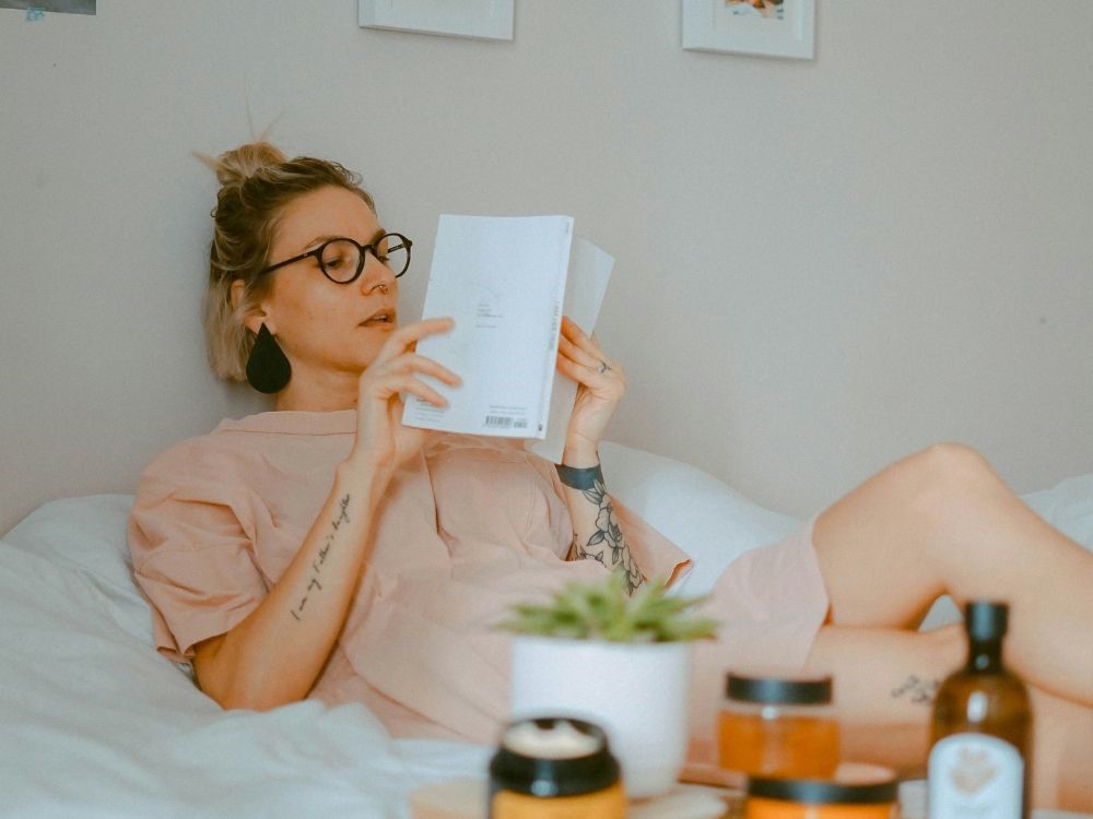 o simples ato de fazer uma leitura é um ato autocuidado que é essencial para o bem-estar feminino. Nesta imagem mulher deitada na cama lendo um livro, um momento de conhecimento e prazer