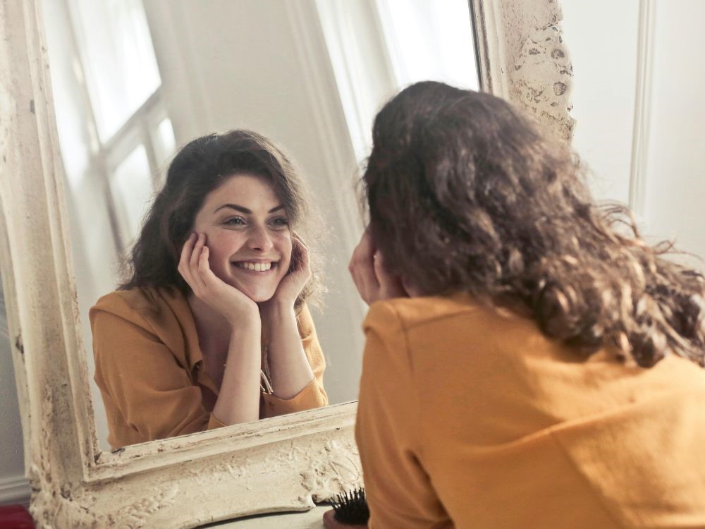 Nessa imagem, mulher radiante e feliz se olhando no espelho. Nesse artigo abordamos a importancia de se sentir importante todos os dias .